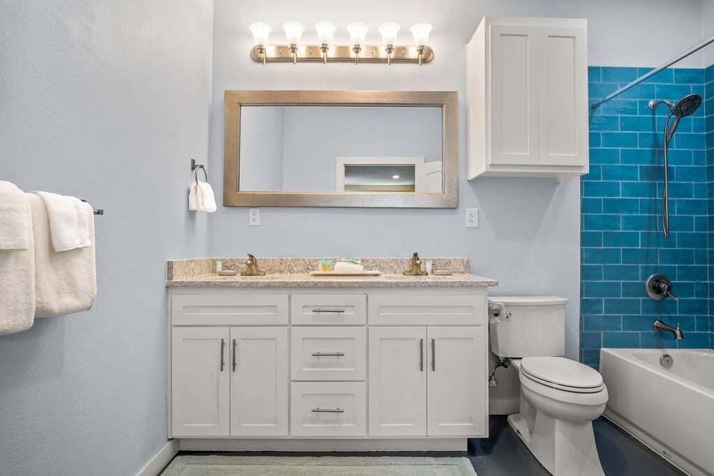 A bathroom with a white vanity, a large mirror, a shower with blue tiles, and a white toilet.