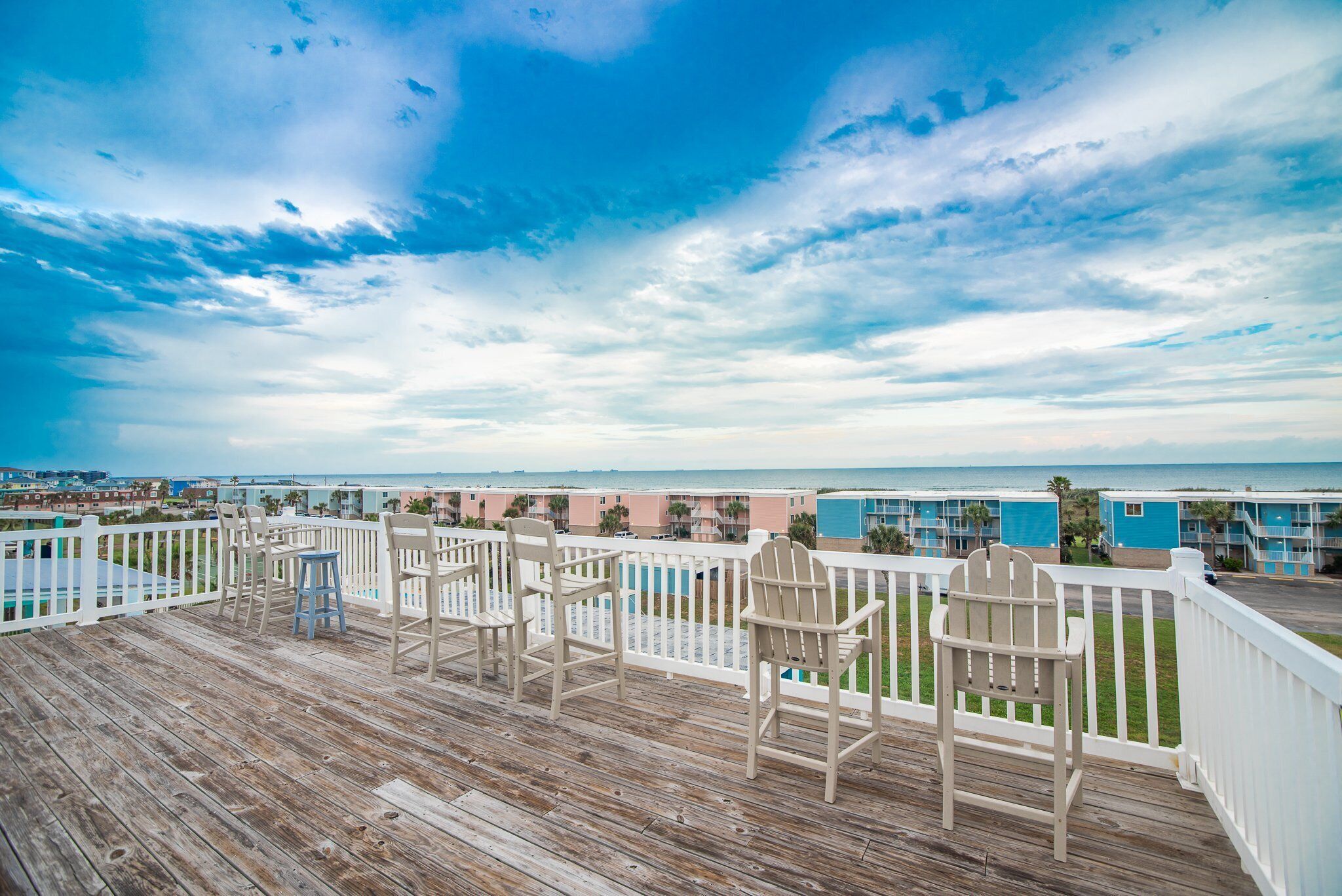A wooden deck with chairs and a table, overlooking a beach with buildings in the background.
