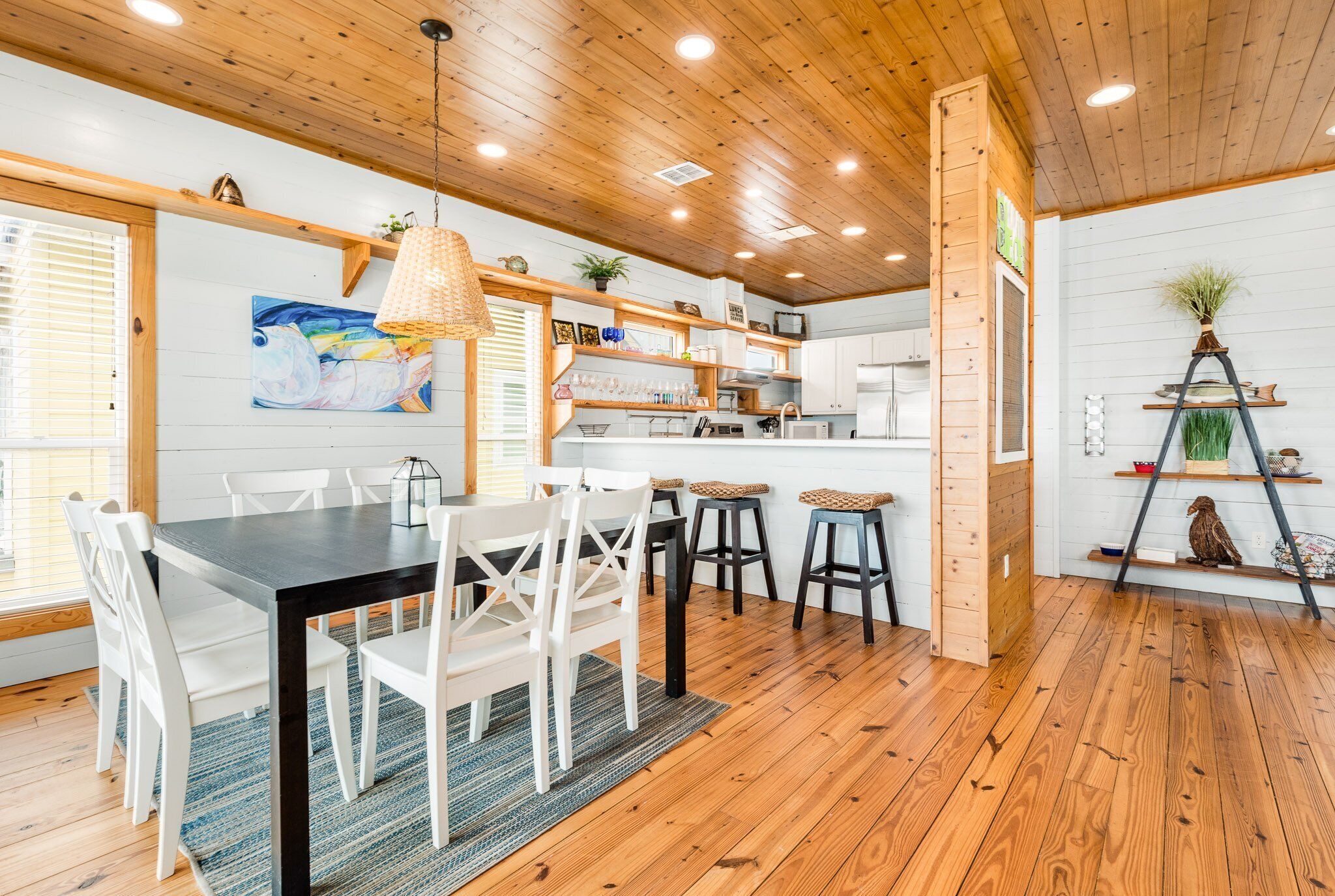 A modern kitchen with wooden floors, white cabinetry, and a dining area with a black table and white chairs.