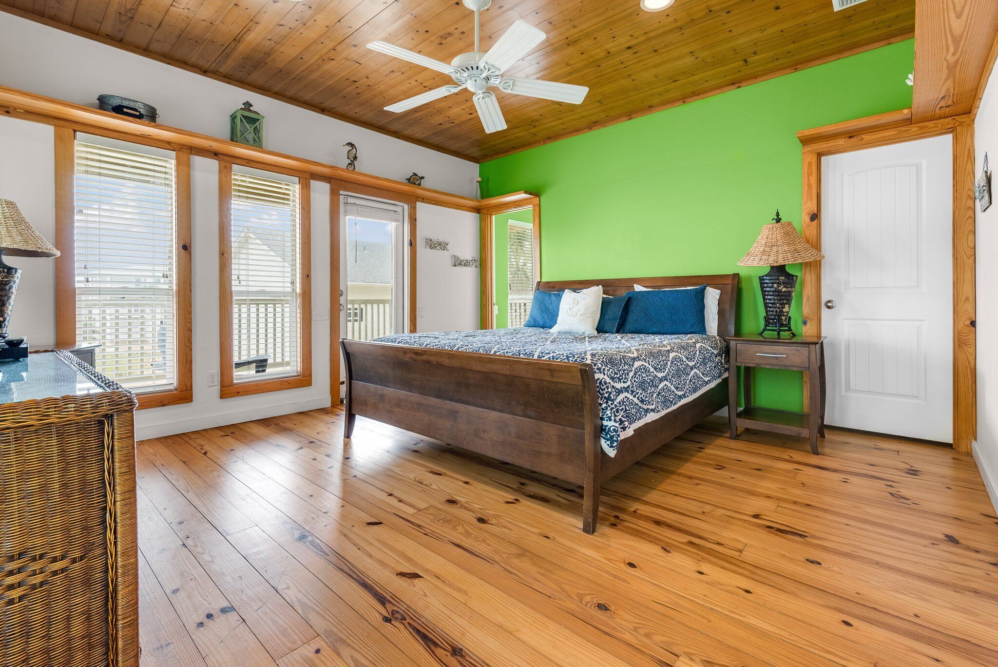 Een slaapkamer met een houten vloer, een bed met beddengoed met een patroon, een plafondventilator en een groene accentmuur.