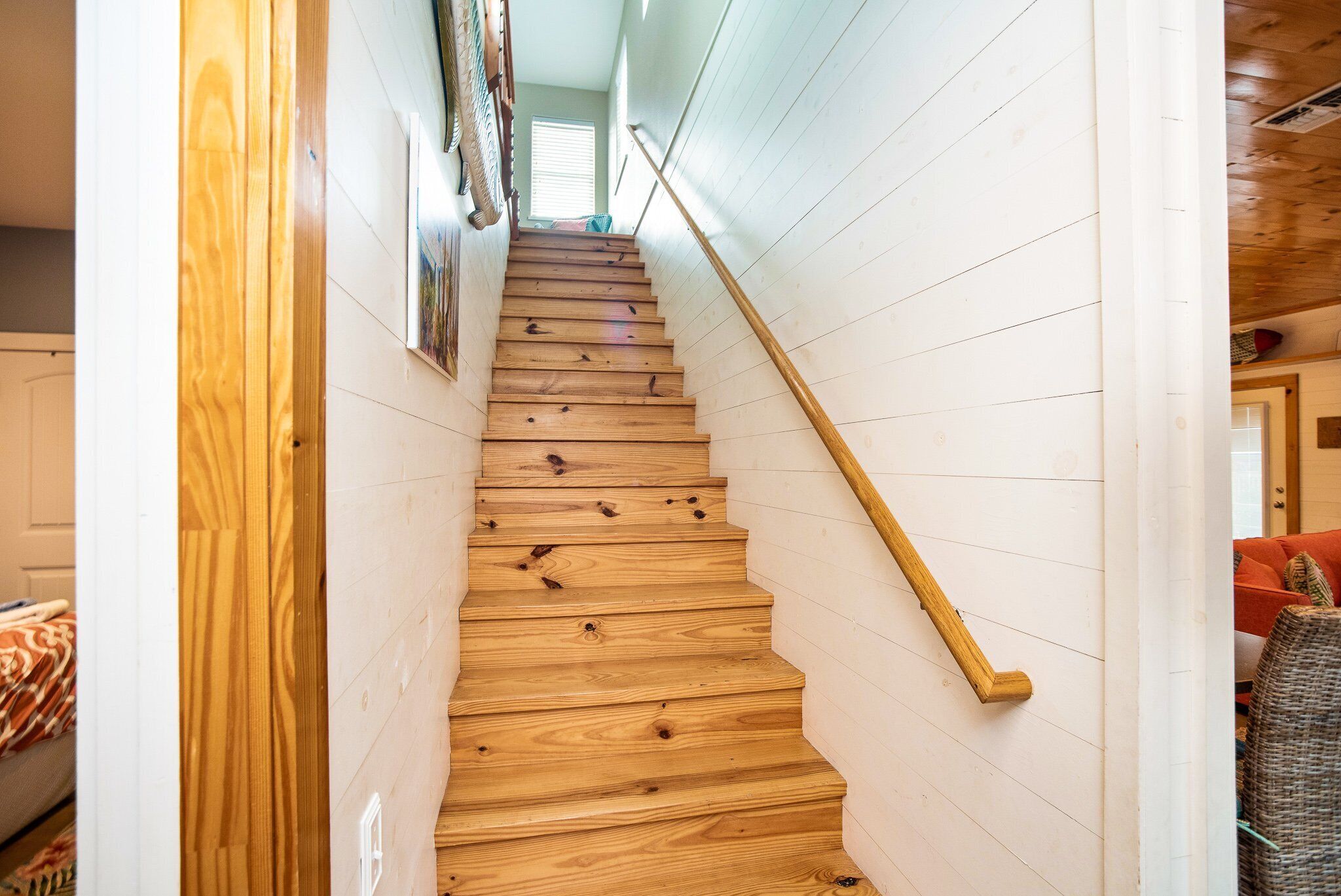 A wooden staircase with a handrail, white paneling on the walls, and a window at the top.