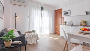 Een moderne woonkamer met een bank, een salontafel met een plant en een eethoek met een tafel gedekt voor twee personen.