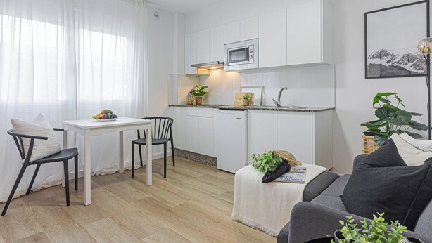Een compacte keuken met witte kastjes, een magnetron en een klein zitehoekje met een tafel en stoelen.