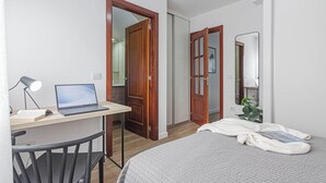 Een slaapkamer met een bed, een bureau met een laptop, een stoel en een spiegel.