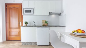 Een kleine keuken met witte kastjes, een magnetron, een vaatwasser en een fruitschaal op het aanrecht.