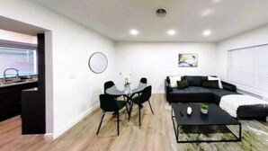A modern living room with a black sofa, a coffee table, and a dining area with a glass table and chairs. - Palm & Paradise Luxe Retreat (Comfort meets City) (Fort Lauderdale)