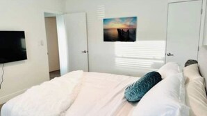 A bedroom with a bed, a TV mounted on the wall, and a door. - Palm & Paradise Luxe Retreat (Comfort meets City) (Fort Lauderdale)