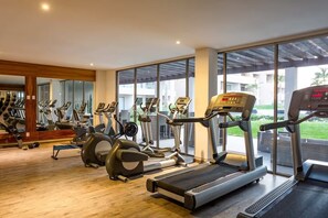 A modern gym with various cardio machines, large windows, and a wooden floor. - Luxury Studio in Cabo San Lucas! Great Location, Pool, Gym & Paddle Court Access (Cabo San Lucas)