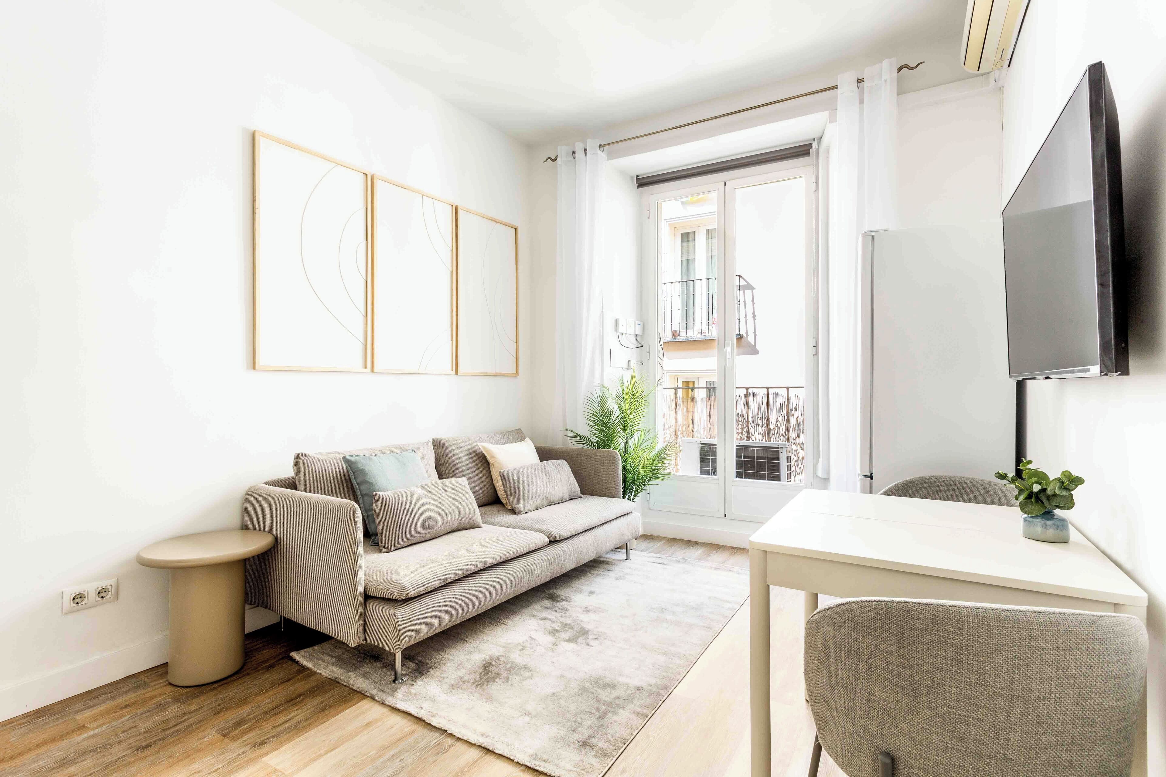 A modern living room with a sofa, a small round table, a TV, and a balcony view.