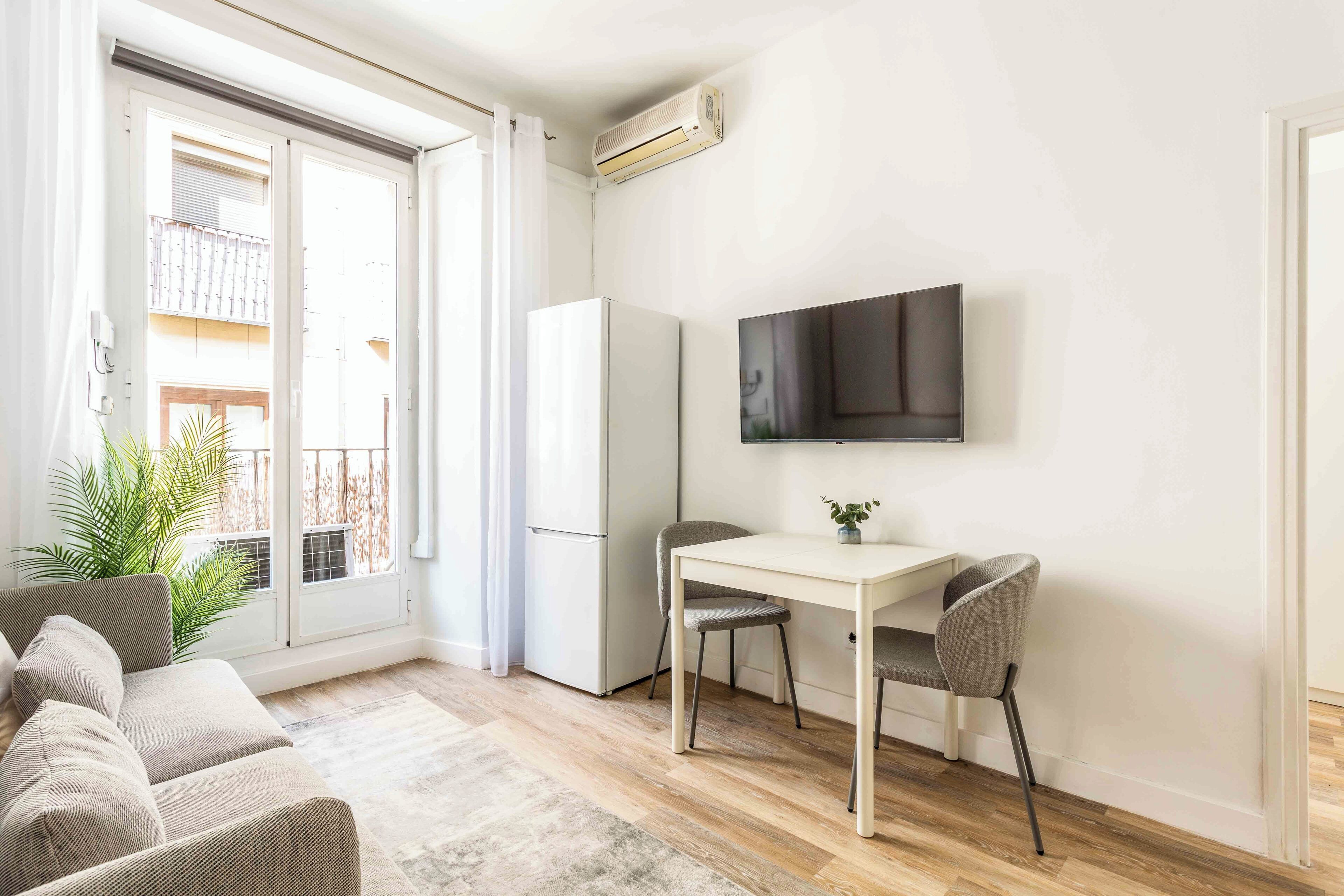 Ein modernes Wohnzimmer mit einer Couch, einem Esstisch mit Stühlen, einem flachbildfernseher an der Wand und einer Glastür zum Balkon.