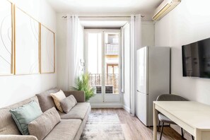 En moderne stue med sofa, spisebord og et fjernsyn oph ængt på væggen.