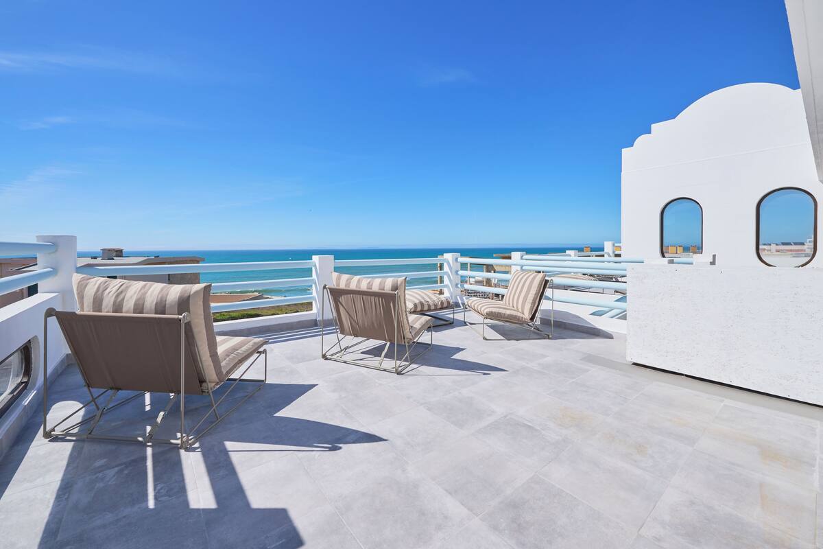 Una terraza con dos sillones acolchados y una mesa, con vistas al mar azul y despejado.