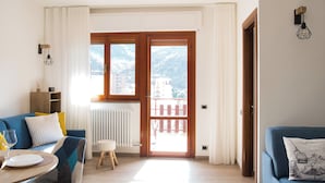 A modern living room with a sofa, a small table, and a view of a mountain through a large window. - La Terrazza di Aurora (Cremeno)
