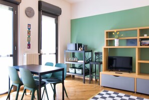 A room with a table, chairs, a television, and shelves with items.