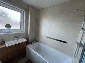 A bathroom with a bathtub, a window with frosted glass, a mirror, and a shower area. - Edinburgh Home from Home (Edinburgh)