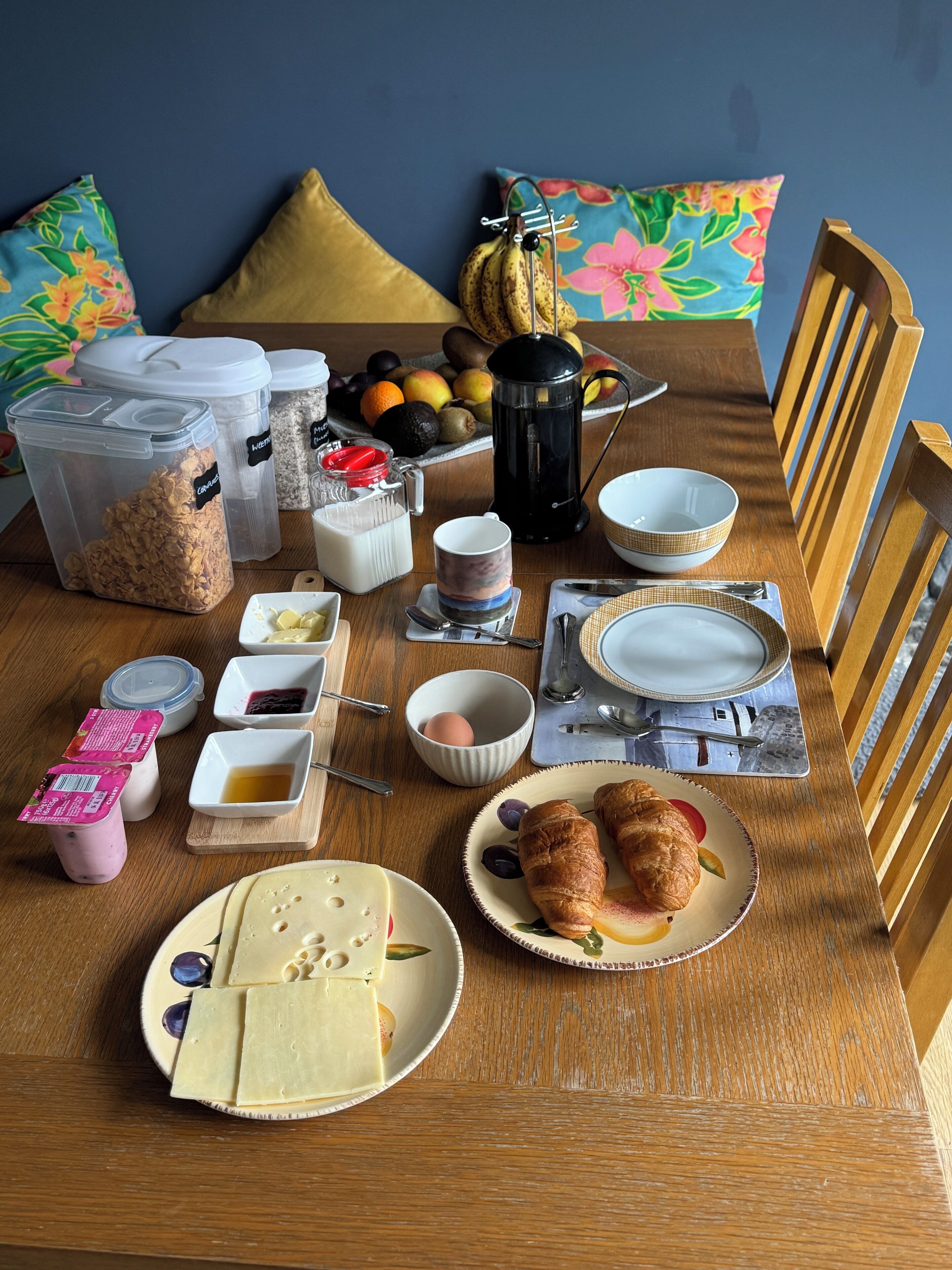 A breakfast table with various food items and containers, including cereal, milk, eggs, and pastries.