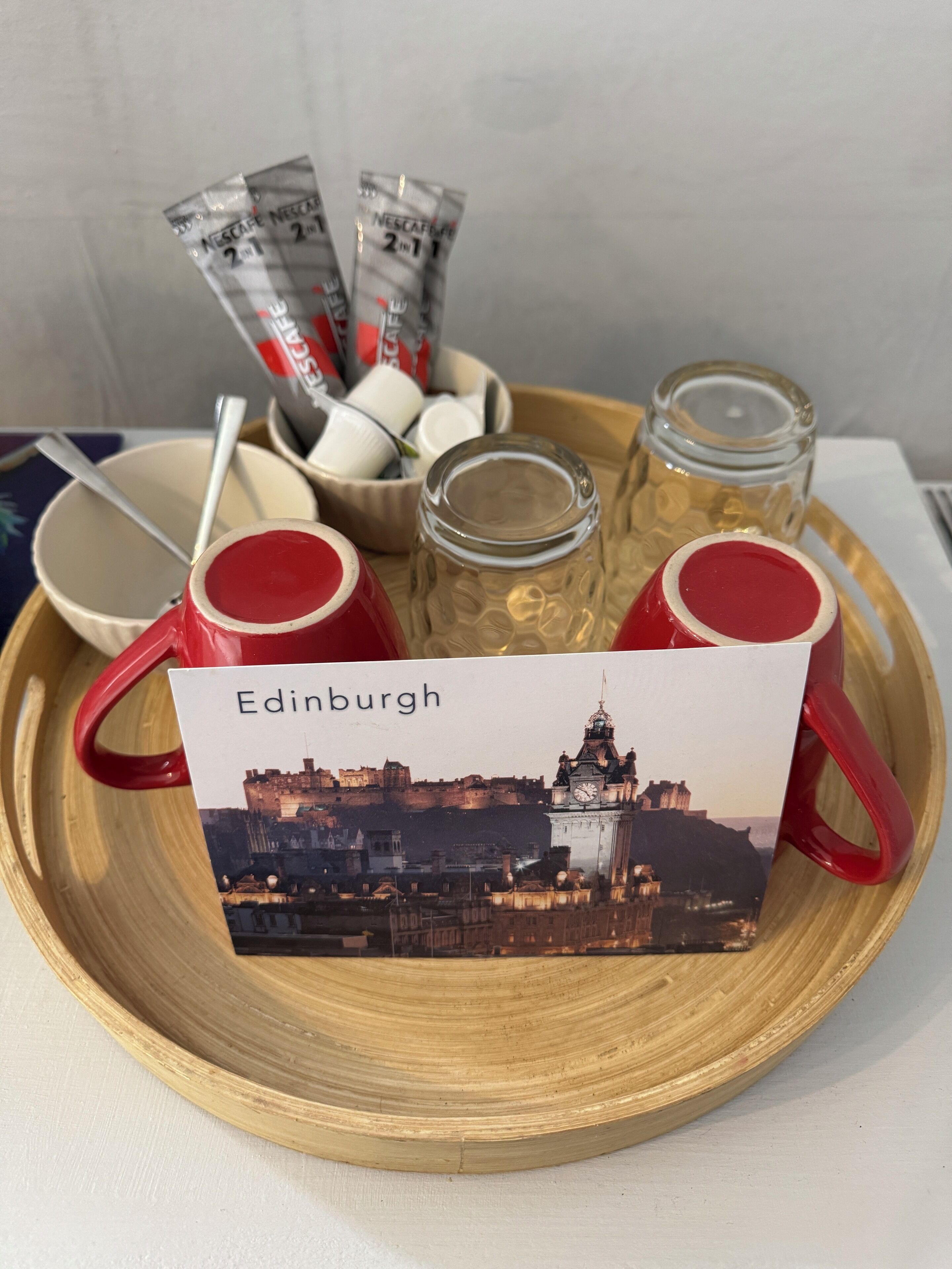 A tray with red mugs, a glass jar, and a card with Edinburgh's skyline.