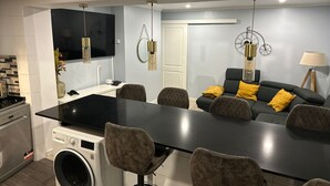 Een moderne keuken met een centraal eiland, een eethoek met stoelen, een bank met kussens en een wasmachine.