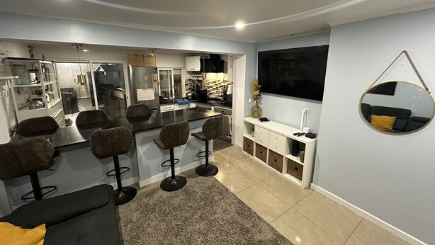 Een moderne keuken met barstoelen, een zithoek met een bank en een grote spiegel aan de muur.