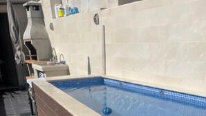 Een rechthoekig buitenzwembad met betegelde rand, een inbouwbank aan één kant en een klein blauw drijvend object in het water.