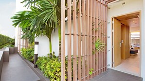 A modern building with a wooden fence, a staircase, and lush greenery including palm trees and shrubs. - Ace of Hua Hin Resort - Ace Junior Suite Pool Access (Cha-am)