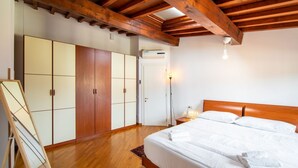 A bedroom with a wooden ceiling, a bed with white bedding, a wardrobe, and a small bedside table with a lamp.