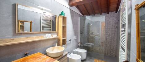 A modern bathroom with a wooden vanity, a large mirror, a freestanding bathtub, a toilet, and a shower enclosure.