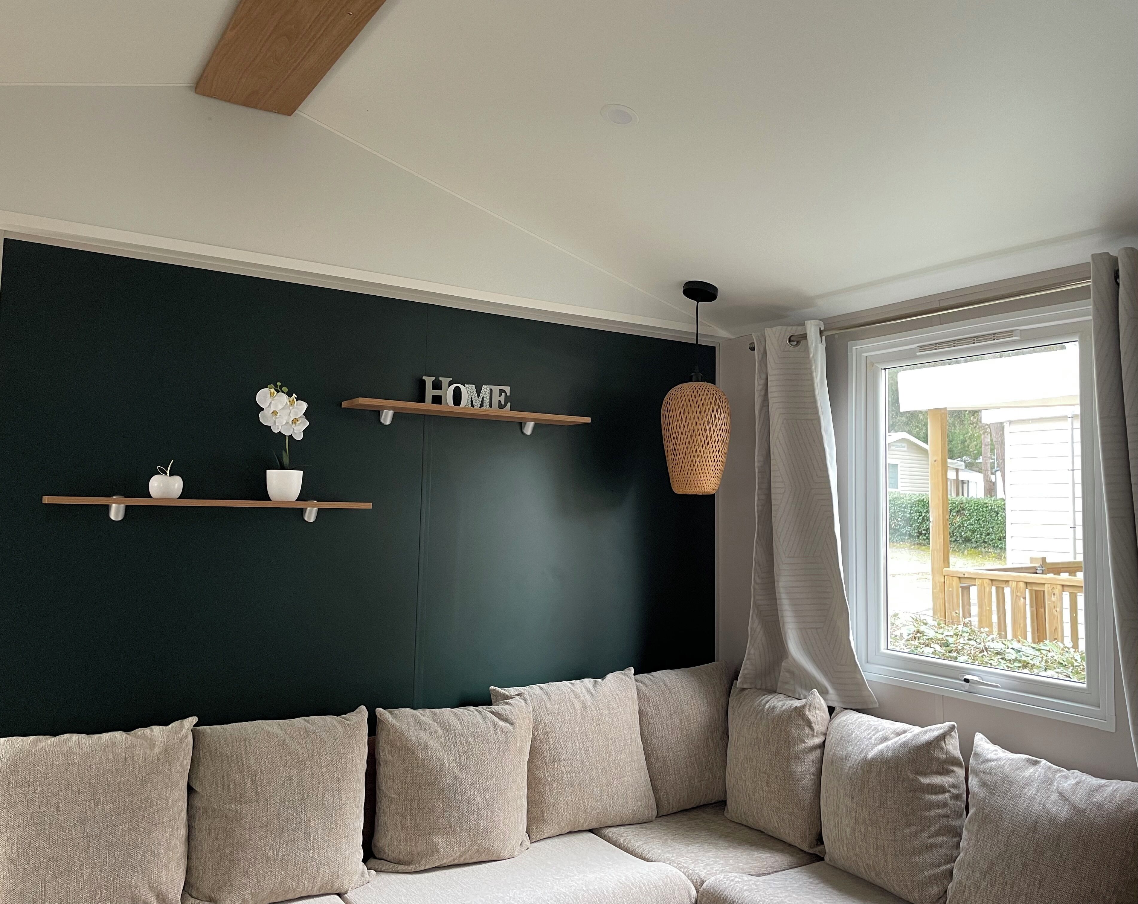 Ein Wohnzimmer mit dunkelgrüner Akzentwand, einem beigen Sofa und einem Fenster mit Blick ins Freie.