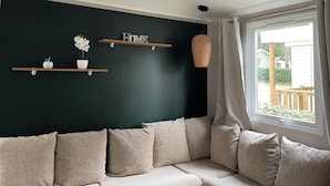 Ett vardagsrum med en mörkgrön accentvägg, en beige soffa och ett fönster med utsikt över omgivningen.