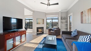 A modern living room with a flat-screen TV, a fireplace, a ceiling fan, a sofa, and a coffee table.