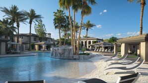 A pool area with lounge chairs, palm trees, and a fountain.