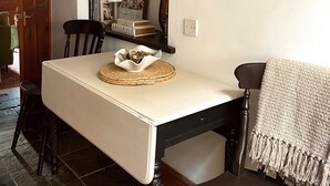 Ein Essbereich mit einem weißen Tisch, schwarzen Stühlen, einer gewebten Tischmatte und einer Uhr an der Wand.