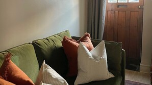 Ein grünes Sofa mit vielen Kissen, ein Gemälde an der Wand und eine Holztür mit Fenster.