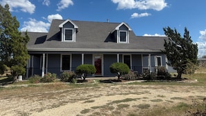 A two-story house with a front porch, a red door, and a small front yard with a gravel path. - Charming 3-bedroom country home (Manor)