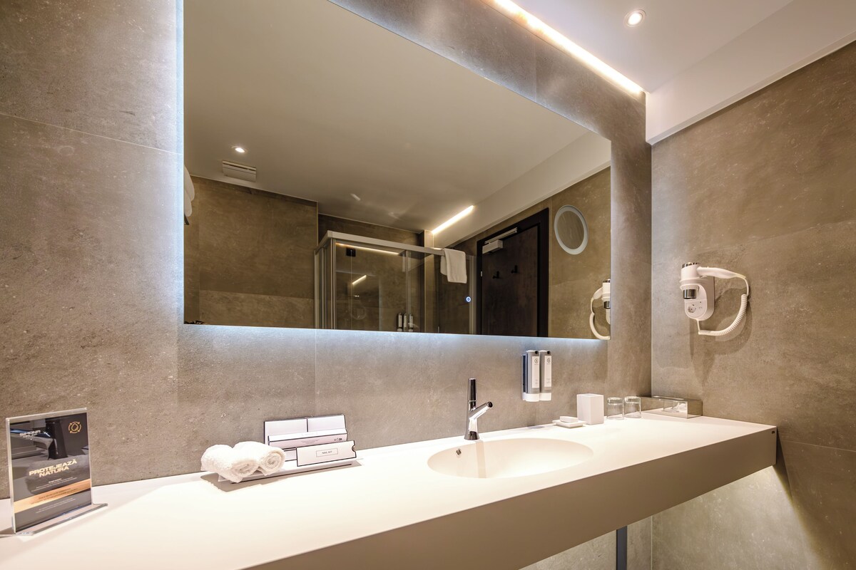 A modern bathroom with a large mirror, a sink, and a hairdryer mounted on the wall.