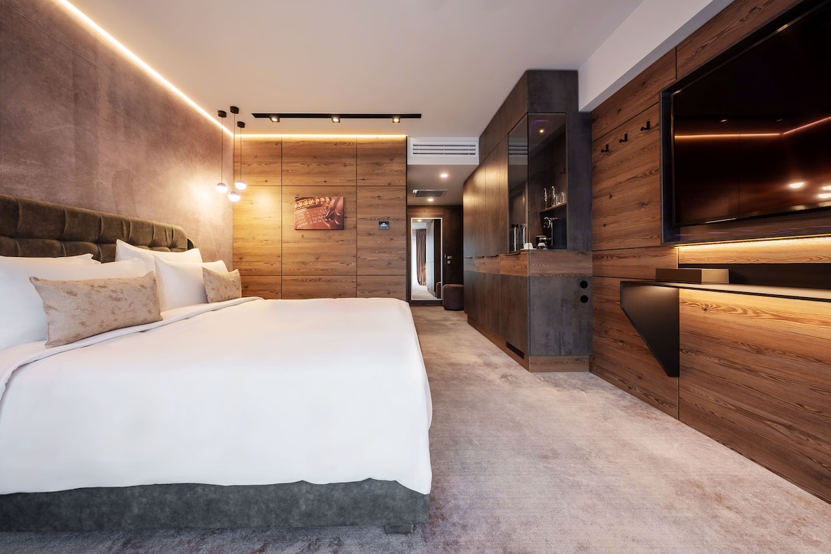 A modern bedroom with a large bed, wooden panel walls, and a built-in TV.