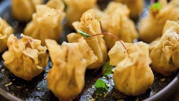 A close-up of a dish with dumplings, garnished with green herbs and a red leaf, served on a dark plate.