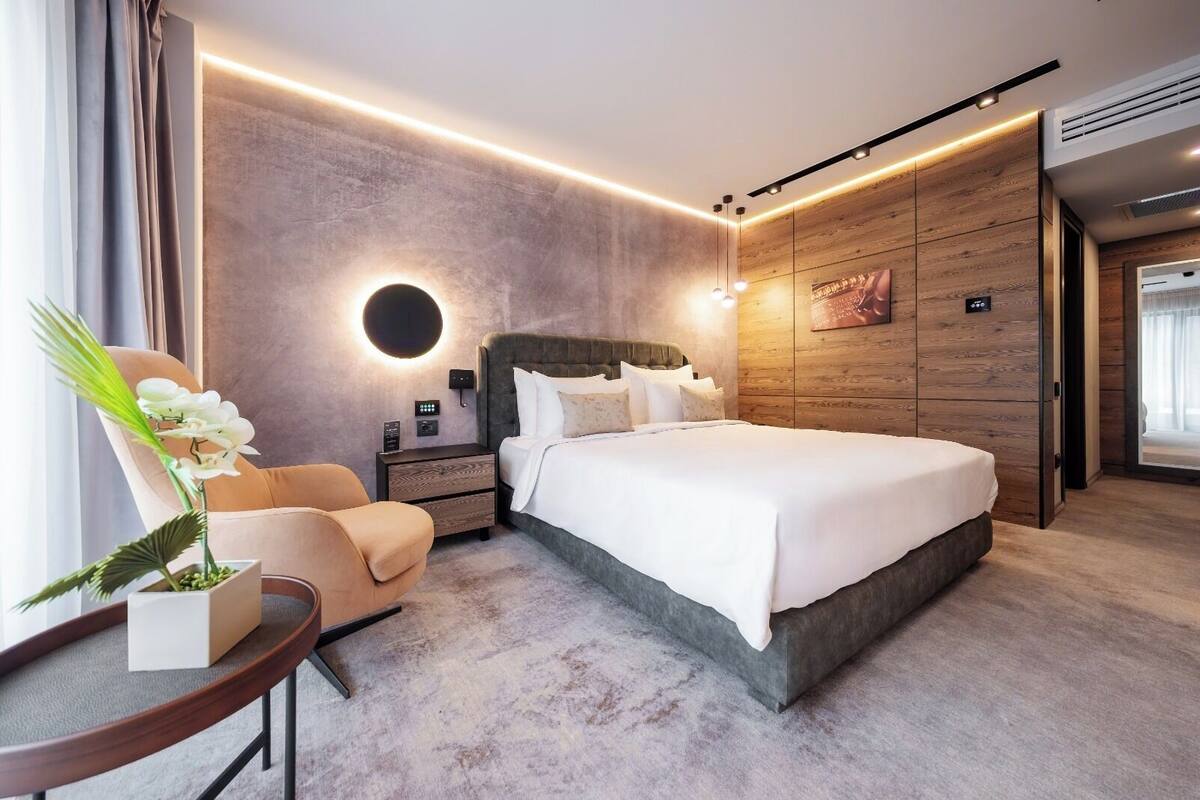 Moderni hotellihuone, jossa on suuri sänky, yöpöytä, tuoli ja pieni pöytä, jonka päällä on kasvi.