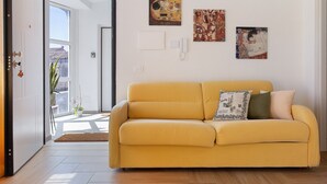 A yellow sofa in a room with a door leading outside, a wall with three paintings, and a small potted plant. - Apartment 'Lu Furru - Carasau' with Air Conditioning (Telti)