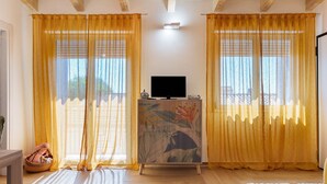 A room with a television on a cabinet, yellow curtains, and a wooden floor. - Apartment 'Lu Furru - Carasau' with Air Conditioning (Telti)