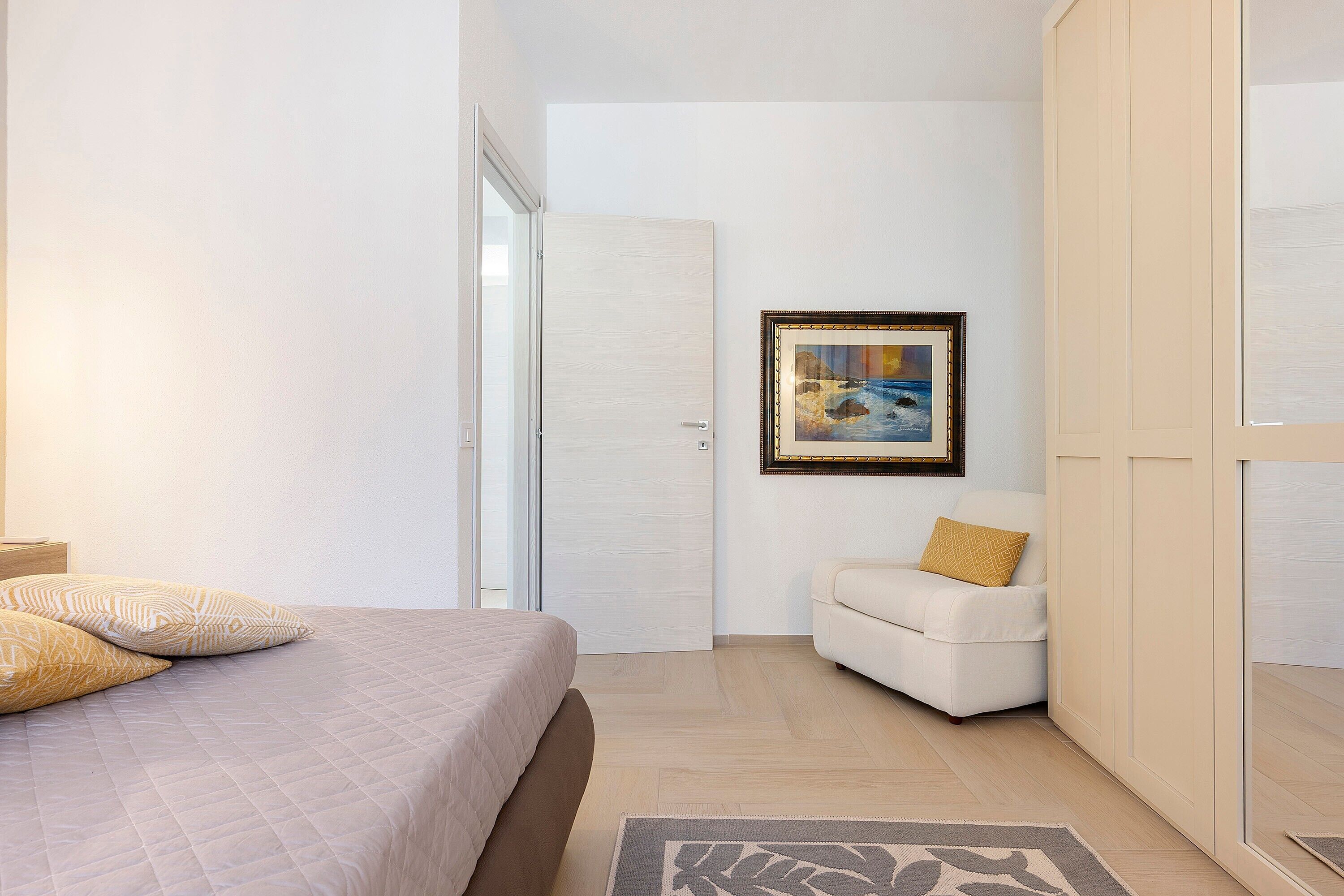 A bedroom with a bed, a chair, a wardrobe, and a painting on the wall.