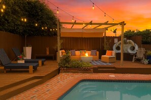 Ein Poolbereich mit Liegestühlen, einer Feuerstelle und einer Pergola mit Lichterketten.