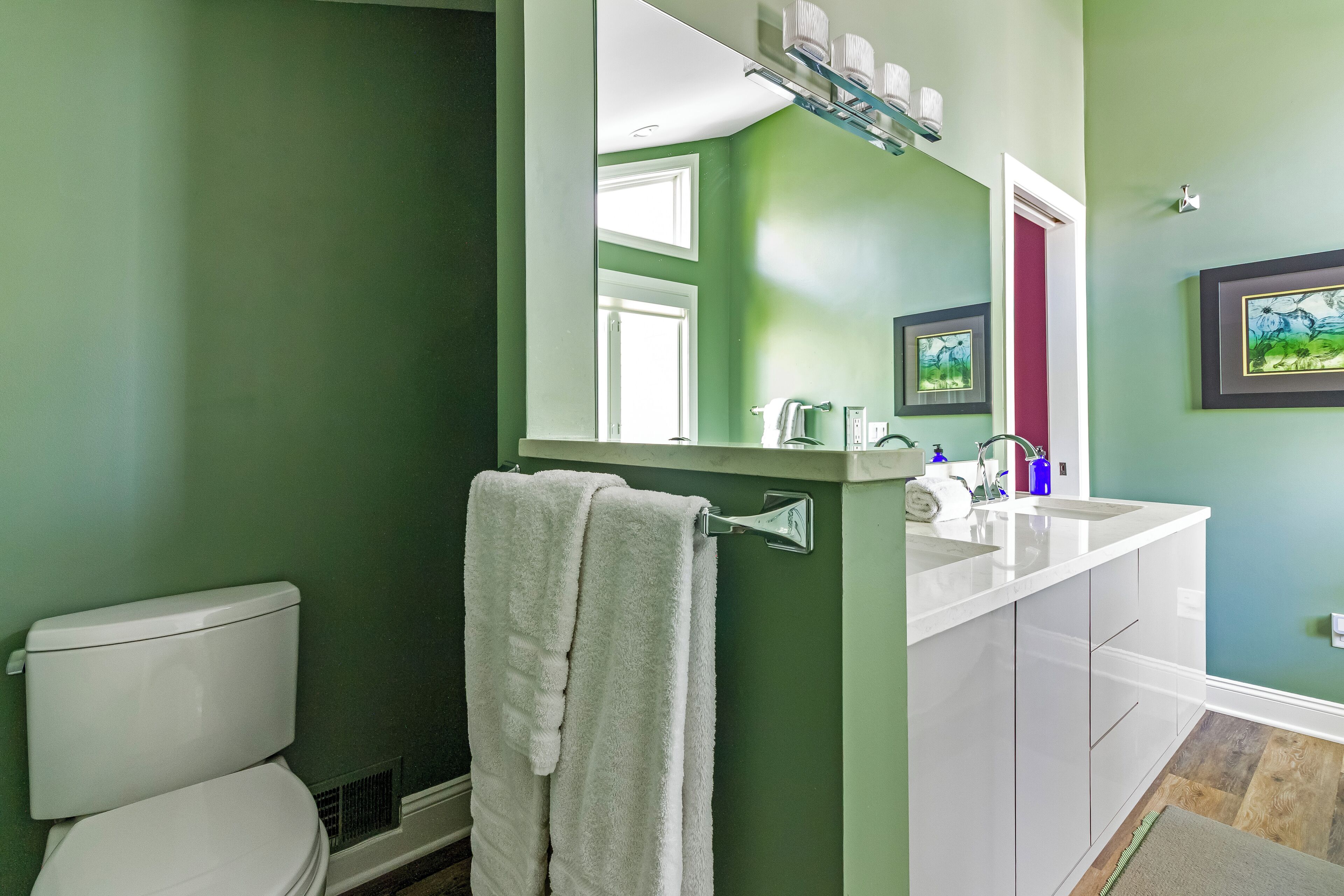 A bathroom with a green wall, white toilet, and a sink with a mirror above it.