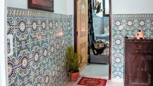Un pasillo con baldosas estampadas, una lámpara colgante, un cuadro enmarcado y un vano que conduce a otra habitación.