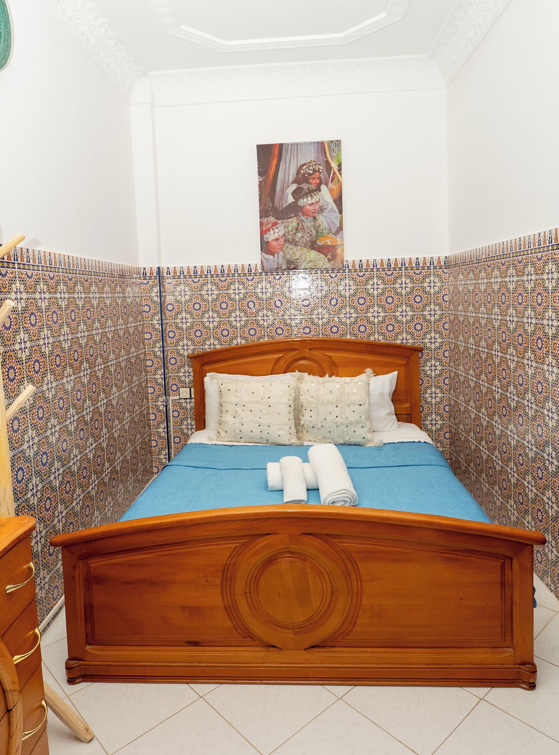 A bedroom with a wooden bed, blue bedspread, and patterned walls.