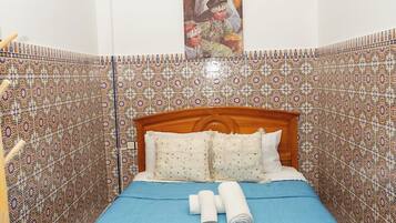 A bedroom with a wooden bed, blue bedspread, and patterned walls.