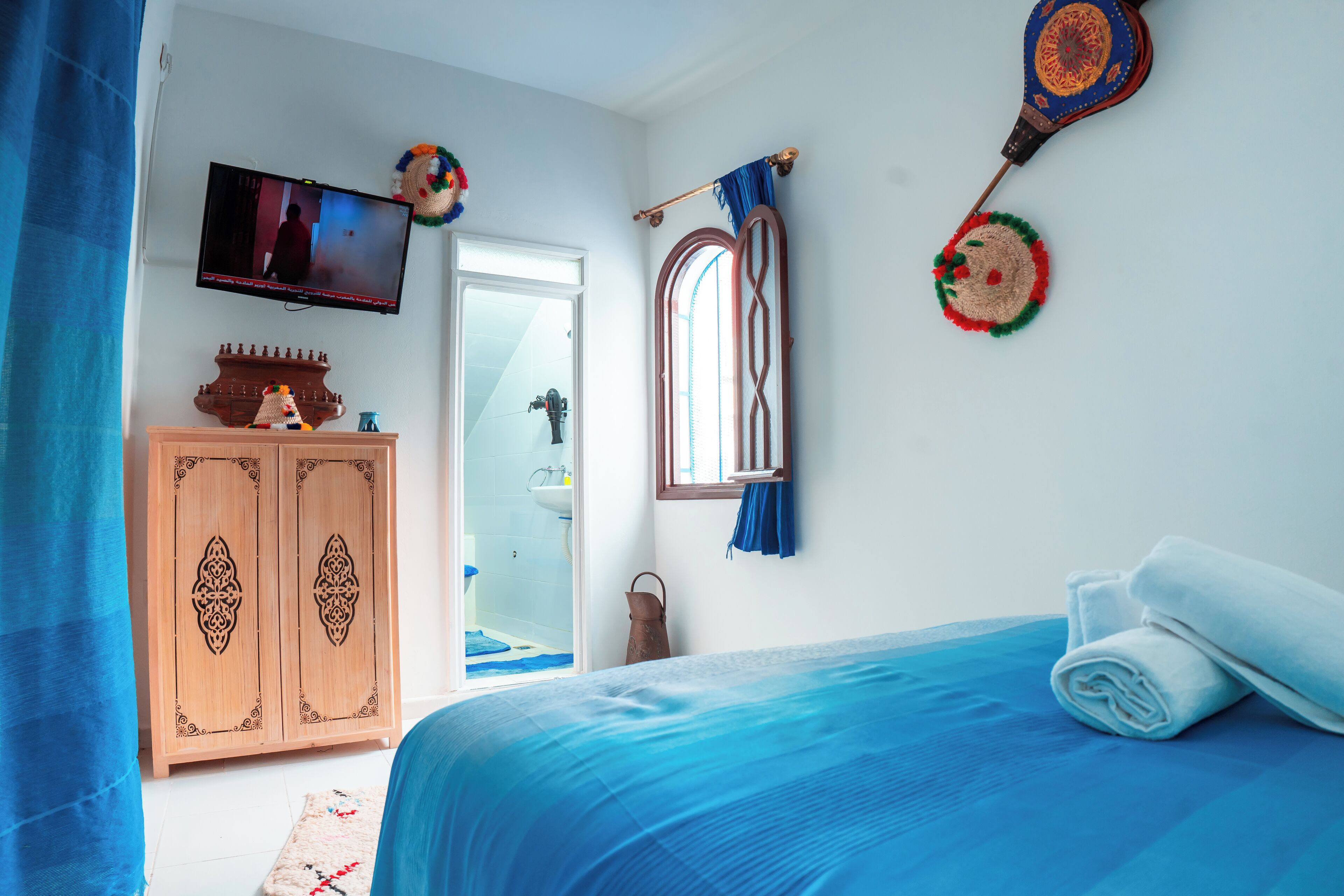 A bedroom with a bed, a TV, a wardrobe, and a window.