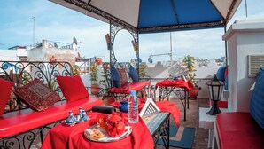 Terraza exterior con asientos rojos y azules, una mesa con tetera y botella de agua, y plantas en macetas.