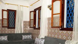 Sala de estar con dos sofás grises, una mesa de centro redonda de madera, baldosas estampadas y una lámpara colgante.