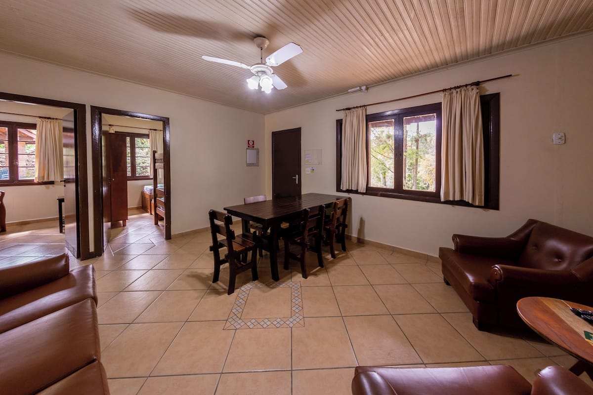 A dining area with a wooden table and chairs, a brown leather sofa, and a ceiling fan.